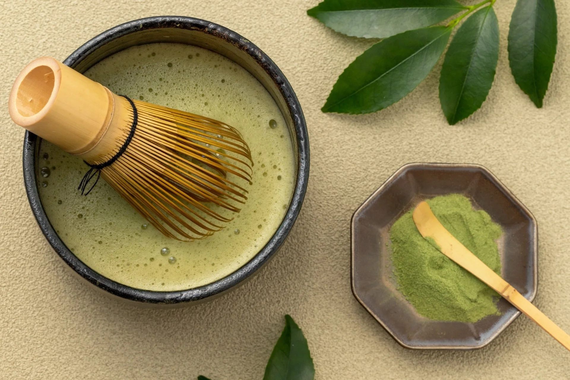 泡立てられた抹茶が入った茶碗に茶筅が置かれ、隣には抹茶粉と茶杓が添えられています。