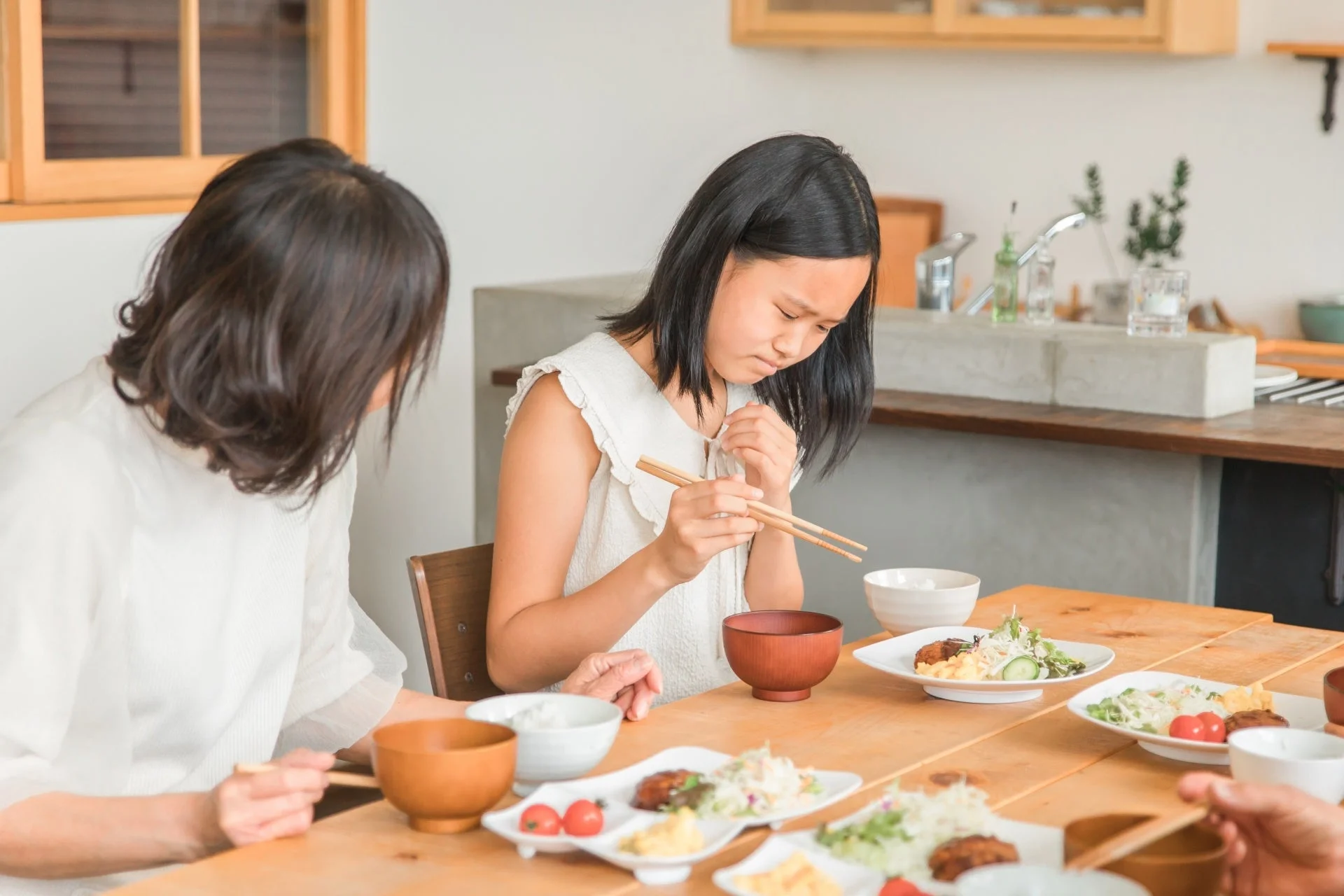 自宅のダイニングで、母親と娘が一緒に食事をしている様子