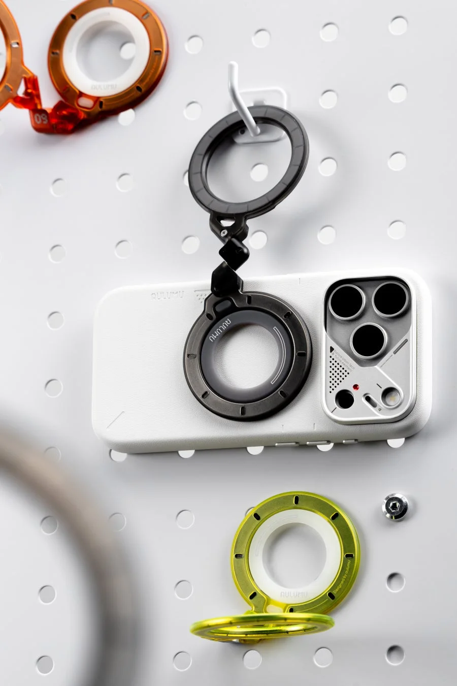 白いペグボードに、ユニークなカメラモジュールとリングアクセサリーが特徴の白いスマートフォンケース