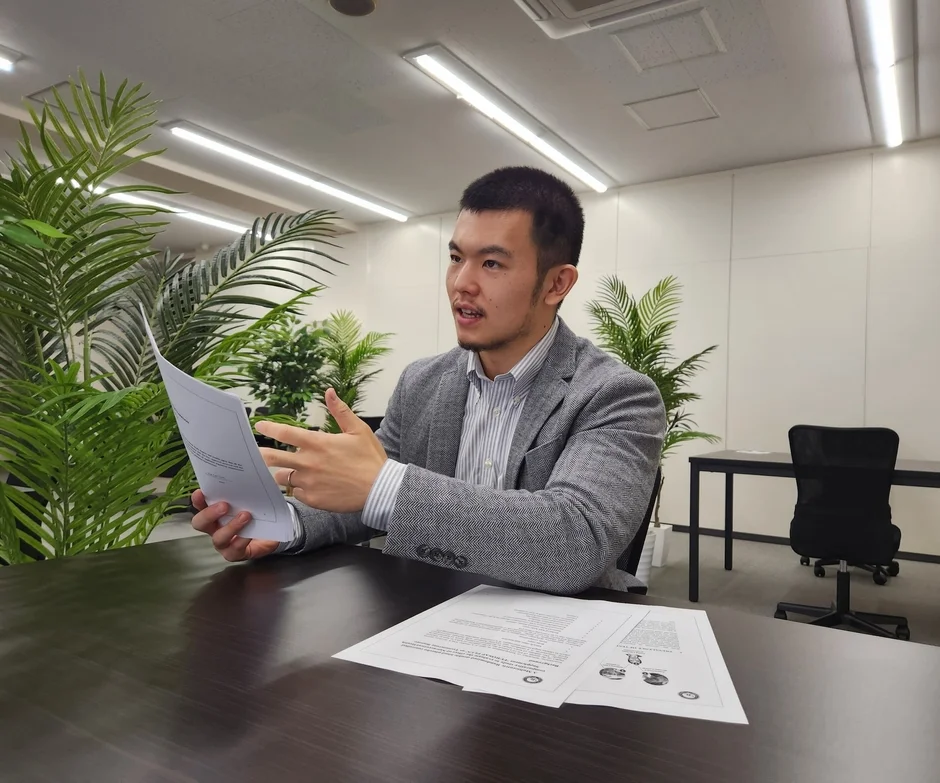 オフィスでスーツ姿の男性が書類を手に持ち、熱心に何かを説明している場面