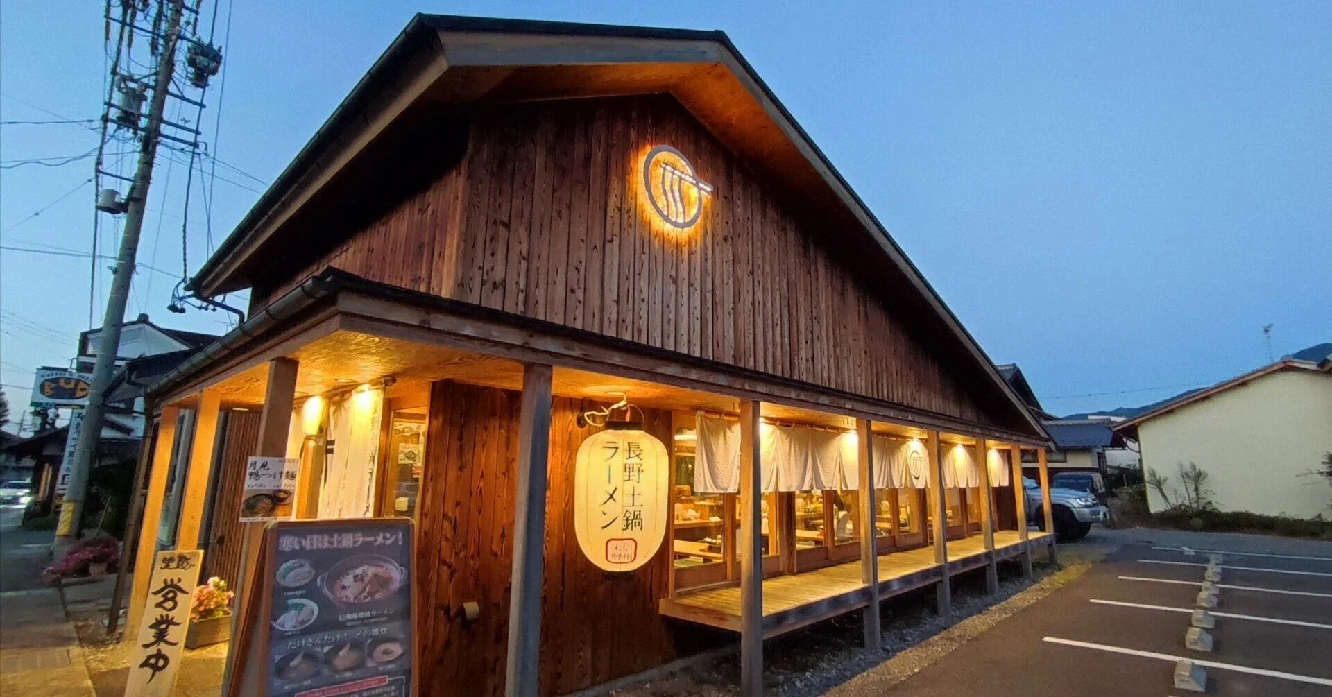 夕暮れ時、温かくライトアップされた木造のラーメン店「長野土鍋ラーメン 吟醸」の外観です。