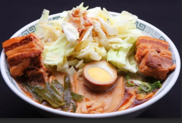 大きなチャーシュー、山盛りのキャベツ、味玉が特徴的な、具材たっぷりのラーメンのクローズアップです。食欲をそそる豊かな盛り付けが目を引きます。