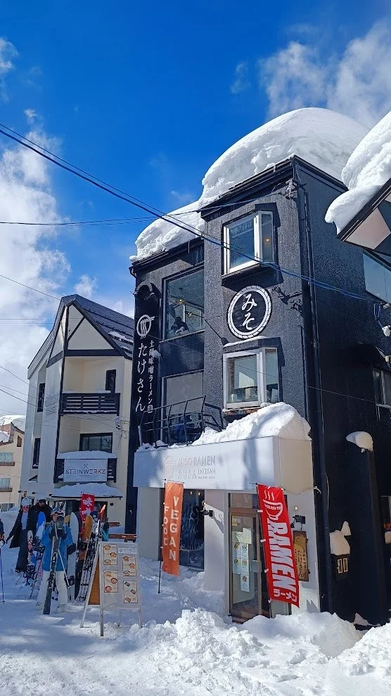 雪が深く積もった日本の冬の街並みで、ラーメン店「MISO RAMEN たけさん」が目立ちます。