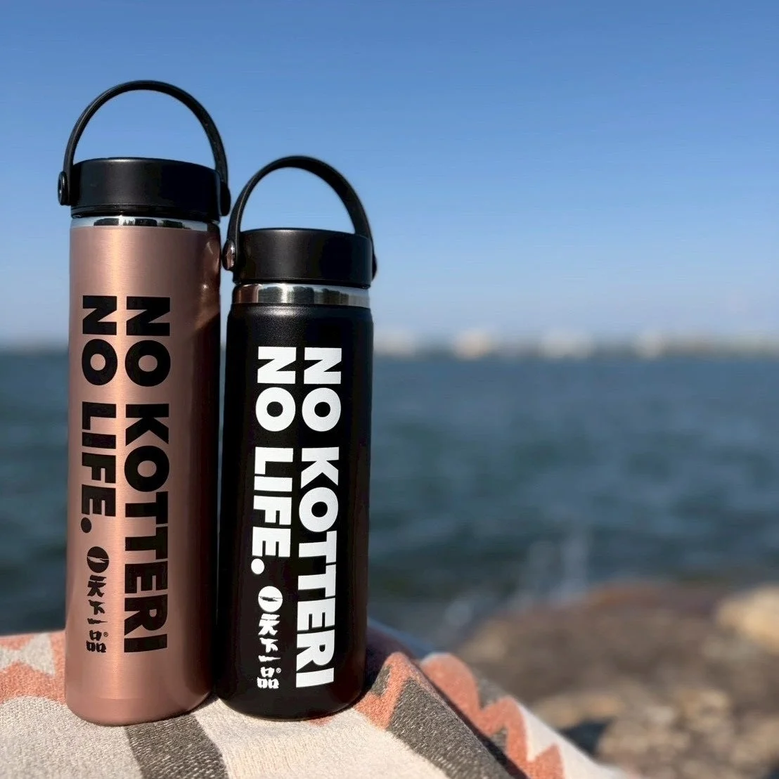 青い空と海を背景に、ブランケットの上に「NO KOTTERI NO LIFE.」と書かれた2つの水筒