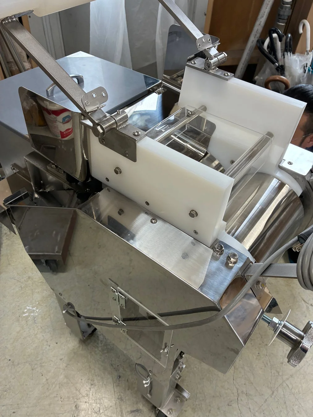 ステンレス製の業務用機械が写っています。白いプラスチック部品と多数の金属部品で構成されており、食品加工などの製造工程で使用される装置と推測されます。
