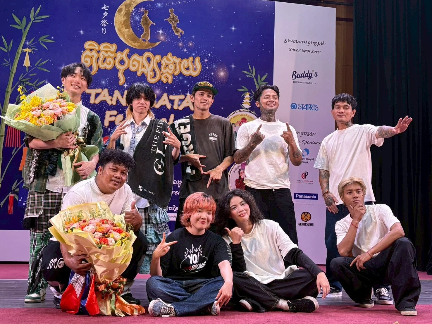 七夕祭りのイベントステージで、花束を持った若者たちがポーズをとっている集合写真です。