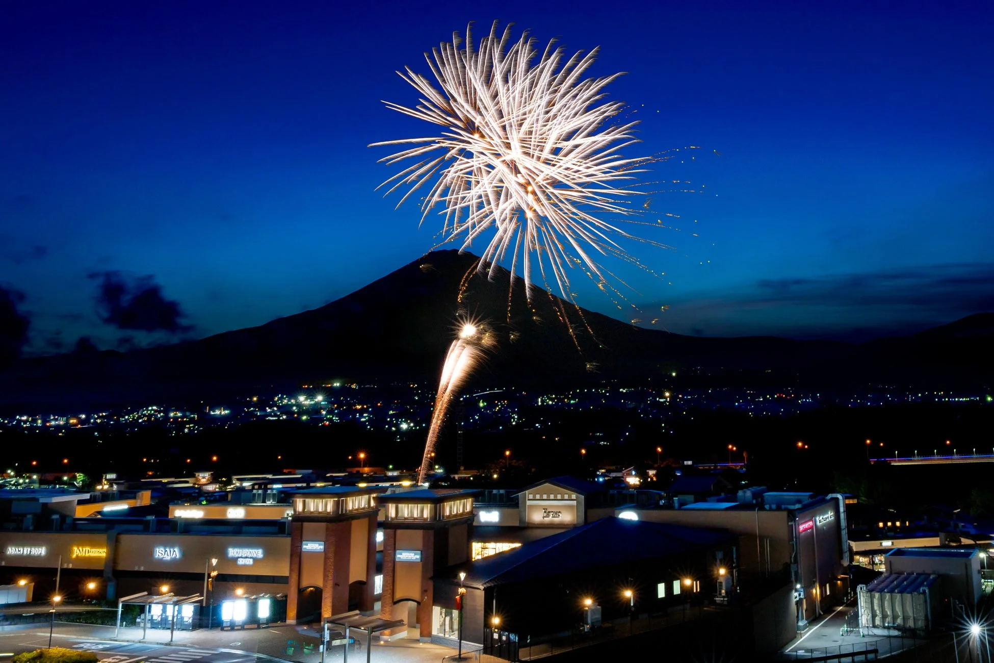 夜空に打ち上がる花火とライトアップされたアウトレット