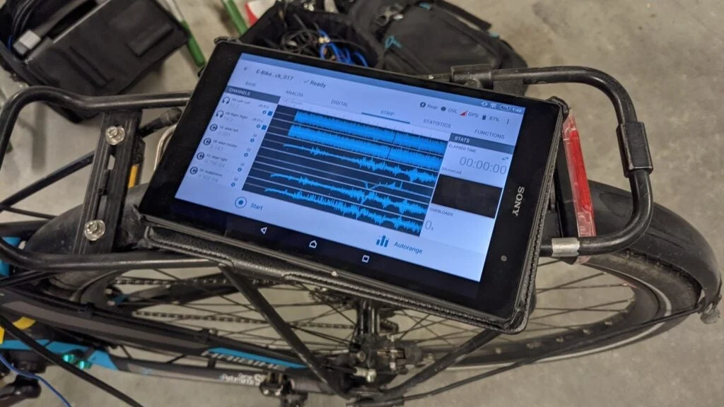 電動自転車のリアラックにSONY製タブレットが取り付けられ、波形や統計データなどの測定結果を表示している様子です。性能分析やデータ収集に使用されていると推測されます。