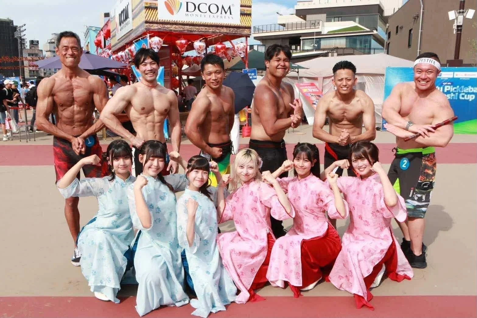 屋外イベントでポーズをとる筋肉質な男性と民族衣装の女性たち