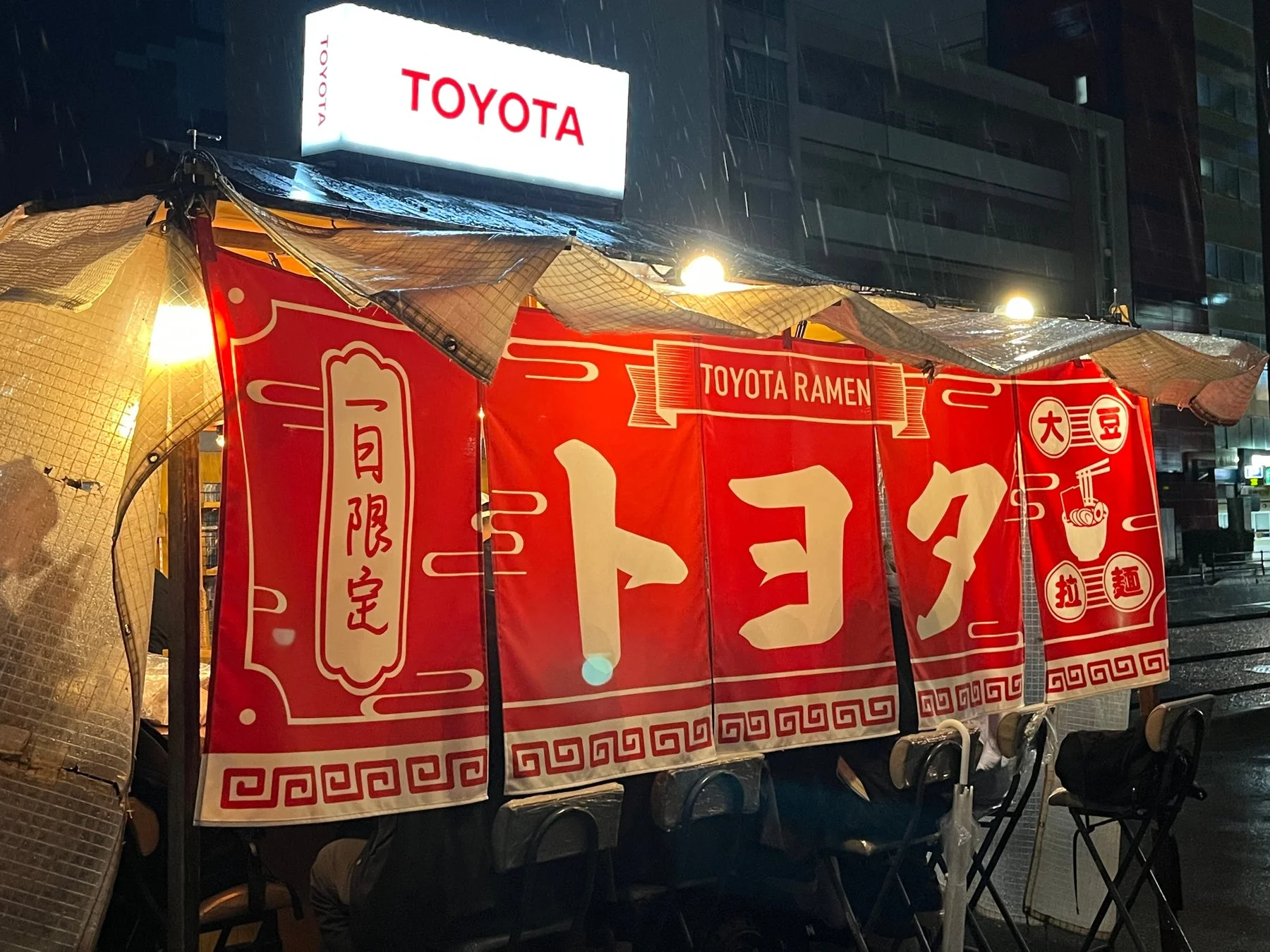 雨の降る夜、屋外に設置された「TOYOTA RAMEN」の屋台