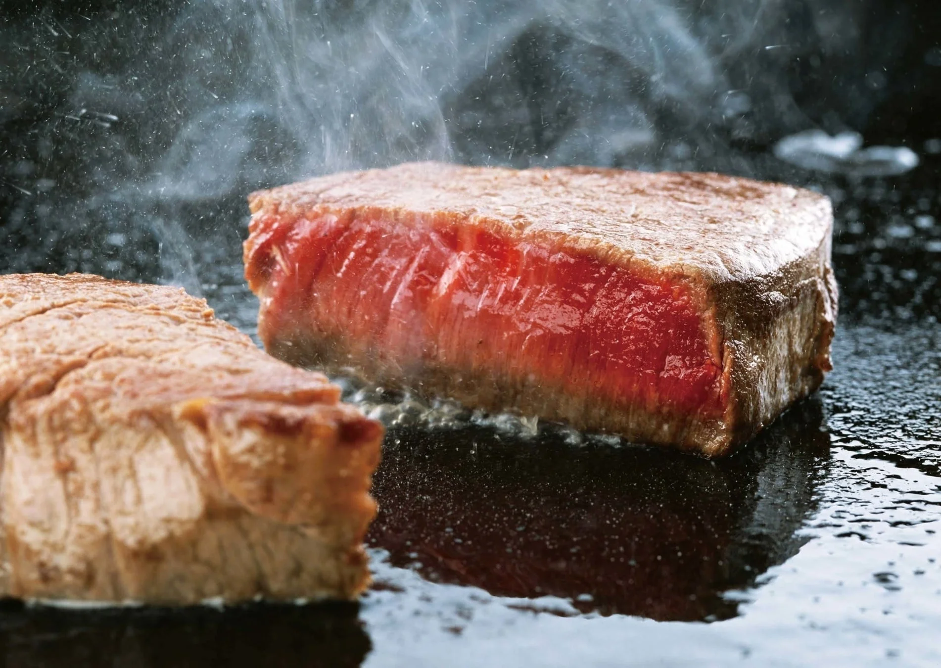 熱い鉄板の上で焼かれる分厚いステーキ肉