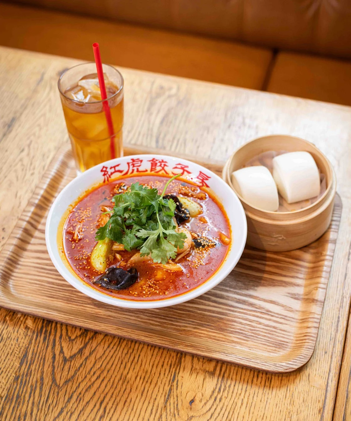 赤いスープの辛そうな麺料理に、蒸しパンとアイスティーが添えられた定食