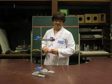 白衣を着た男性が実験器具の置かれたテーブルの前に立つ様子