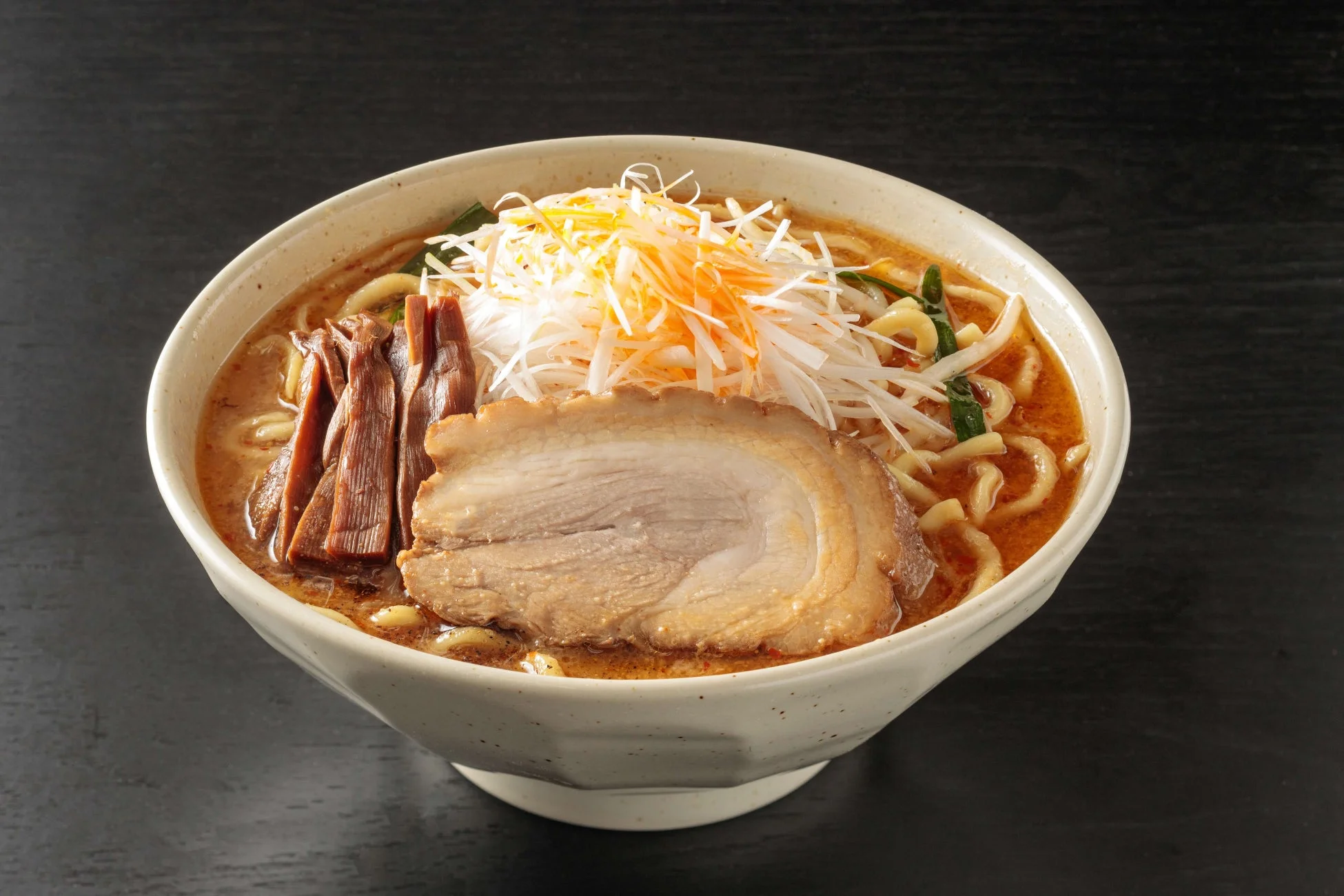 白い器に入った濃厚なスープのラーメン。大きなチャーシュー、メンマ、たっぷりの白髪ねぎが盛り付けられており、食欲をそそる一品です。