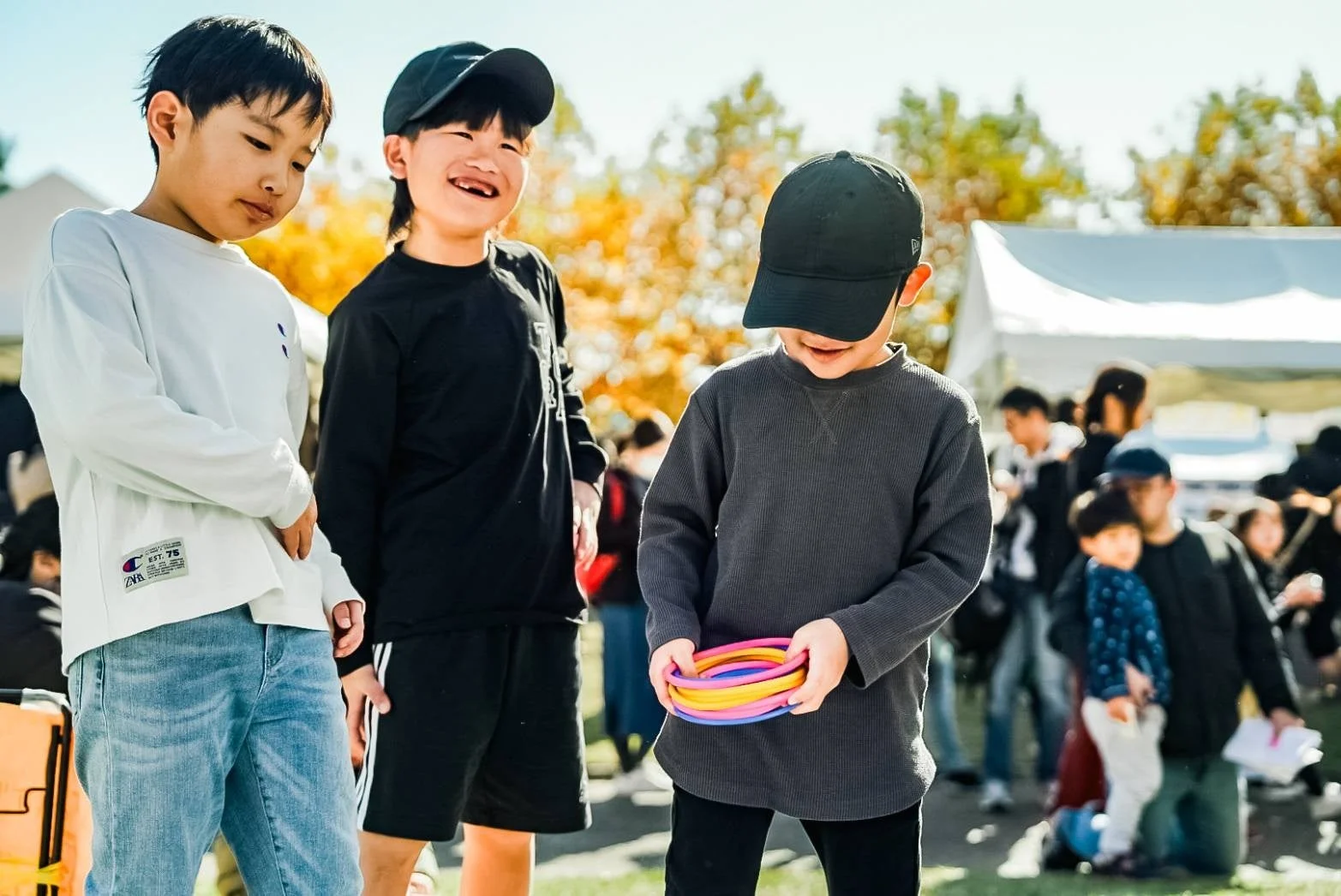 晴れた秋の屋外イベントで、3人の男の子が楽しんでいる様子