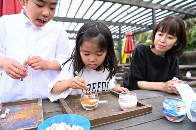 屋外でサンドアートのようなクラフト体験を楽しむ子供たち