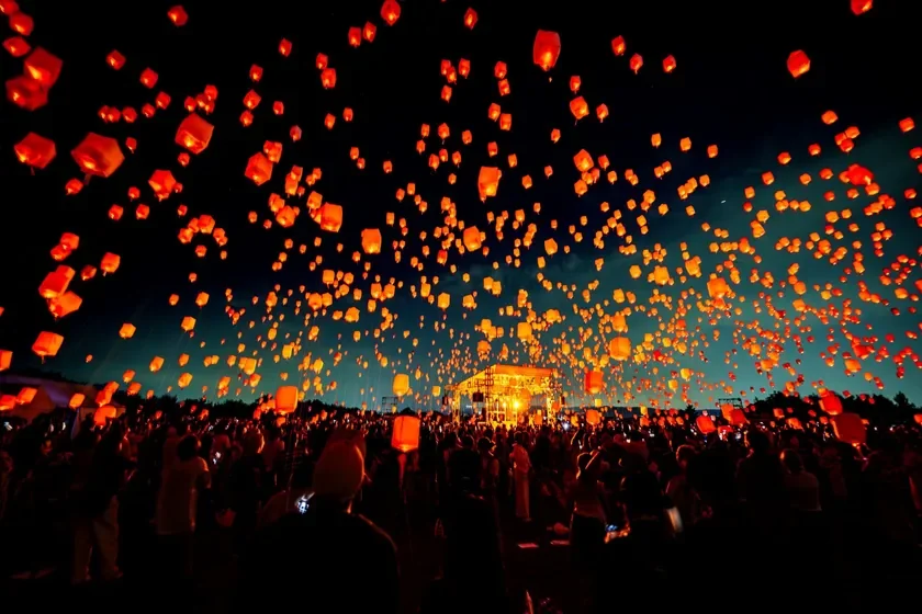 無数のオレンジ色のスカイランタンが夜空を埋め尽くし、ステージと大勢の人々が一体となった幻想的な祭りの光景です。