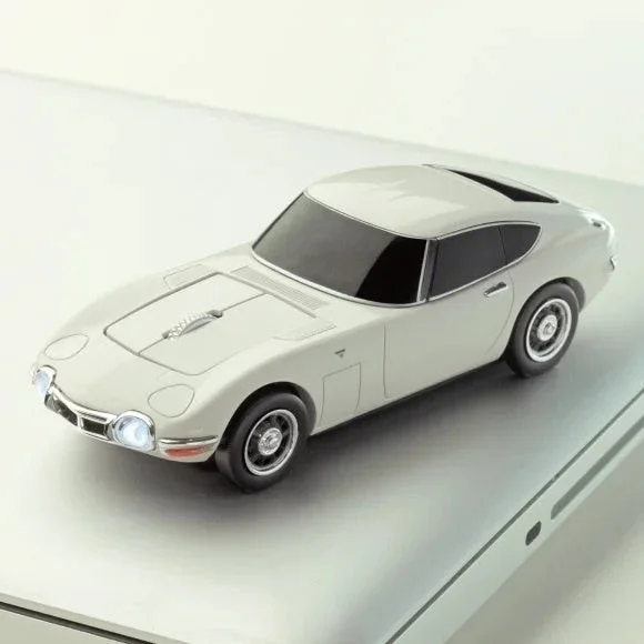 白いクラシックカー(トヨタ2000GT)型のコンピューターマウスが、銀色のノートパソコンの上に置かれている。実用性とデザイン性を兼ね備えたユニークなガジェットの様子。