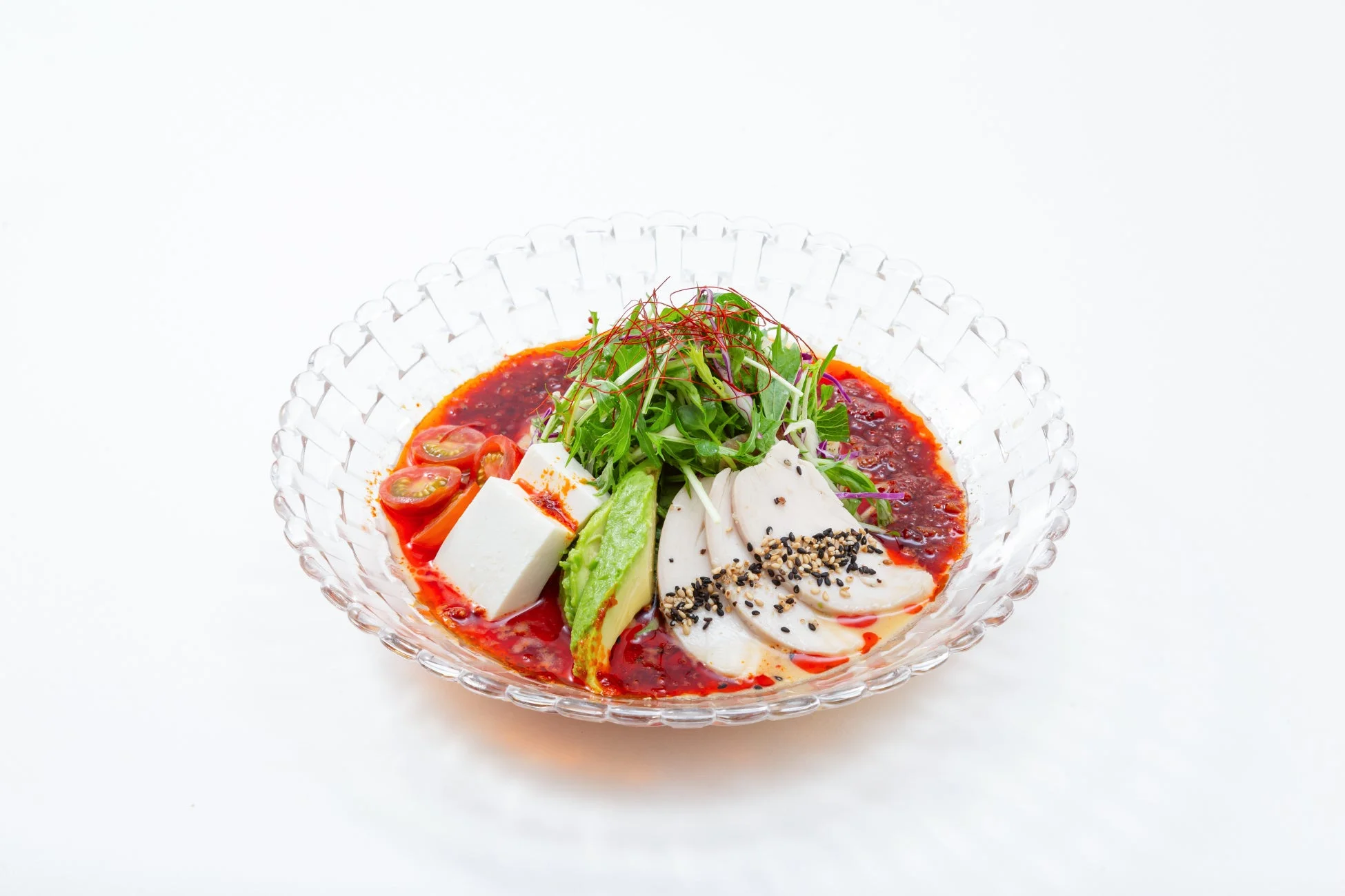 鶏肉、豆腐、アボカド、ミニトマト、水菜などの具材が鮮やかな赤いソースで和えられたヘルシーな冷菜