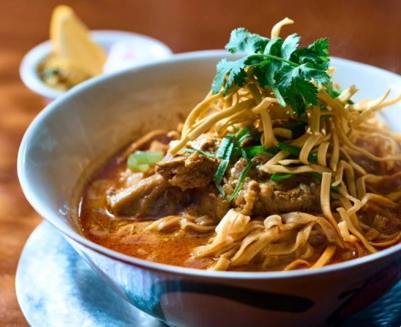 タイの伝統的な麺料理、カオソーイ。クリーミーなカレースープに麺と肉、コリアンダーと揚げ麺がトッピングされている