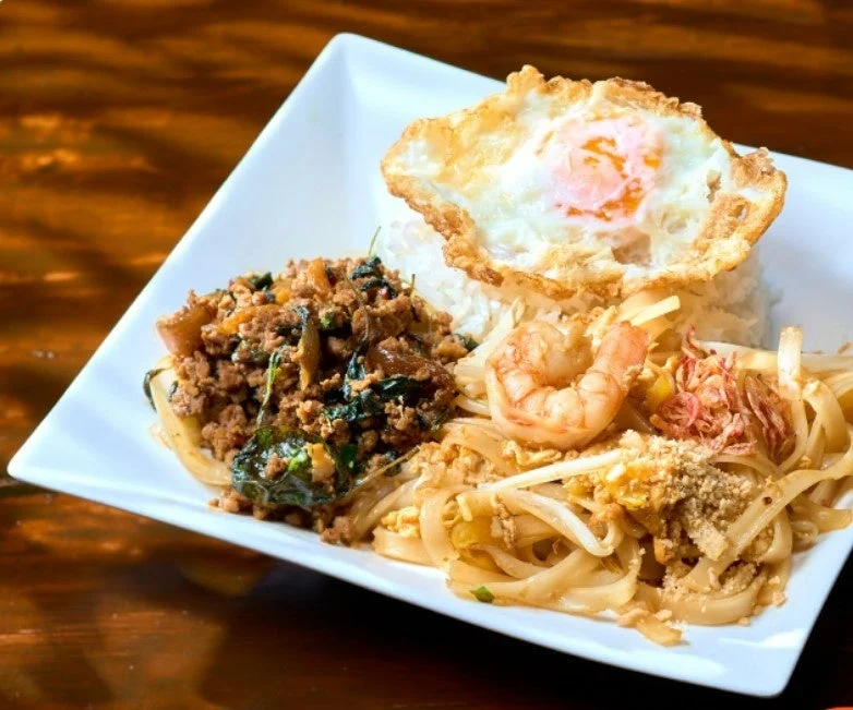 白い皿に盛られたタイ料理のセット。ご飯の上に目玉焼き、ガパオライスのような炒め物、エビとピーナッツが添えられたパッタイ