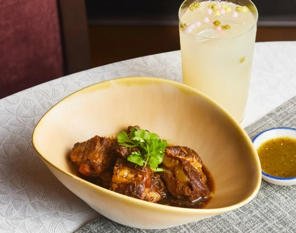 おしゃれな器に盛り付けられた煮込み肉料理と、飾り付けがされたドリンク、緑色のソース