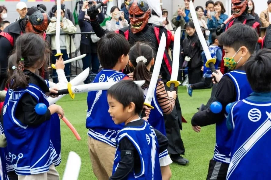 赤い鬼の面をつけた大人が、青い衣装を着ておもちゃの剣を持つ子供たちと交流