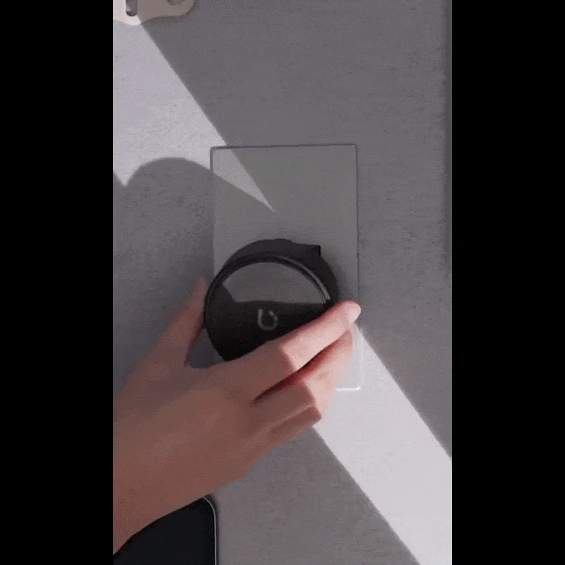 手が壁に取り付けられた黒い丸いスマートデバイスを操作している。室内には陽光が差し込み、デバイスの設置または調整の瞬間を捉えている。