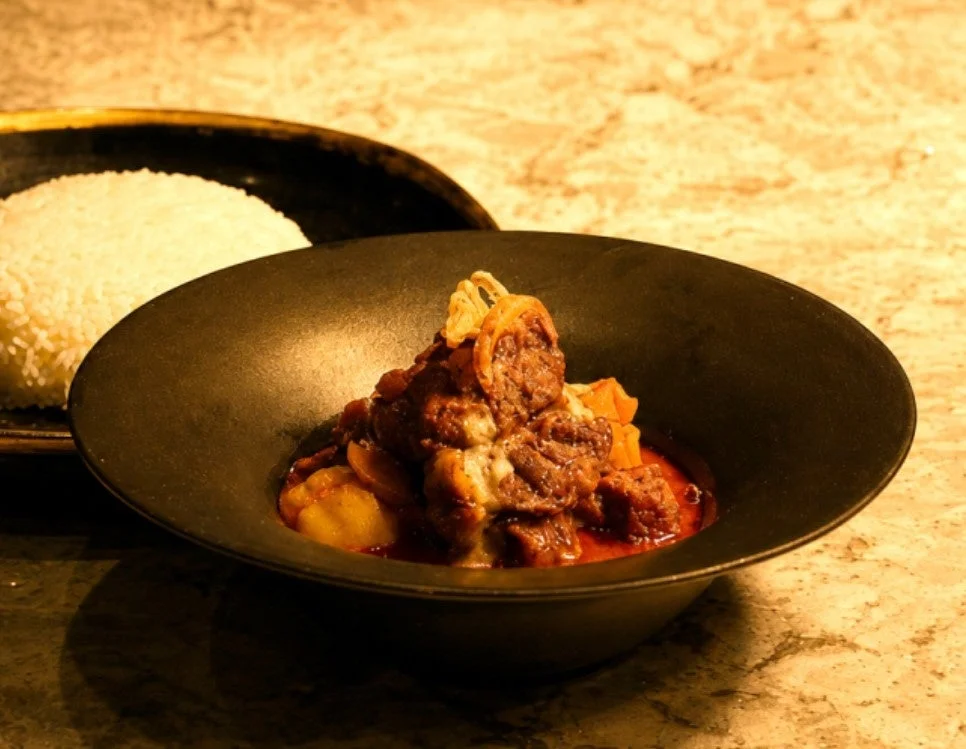 黒い器に盛られた牛肉と野菜の濃厚な煮込み料理(またはカレー)と白いご飯