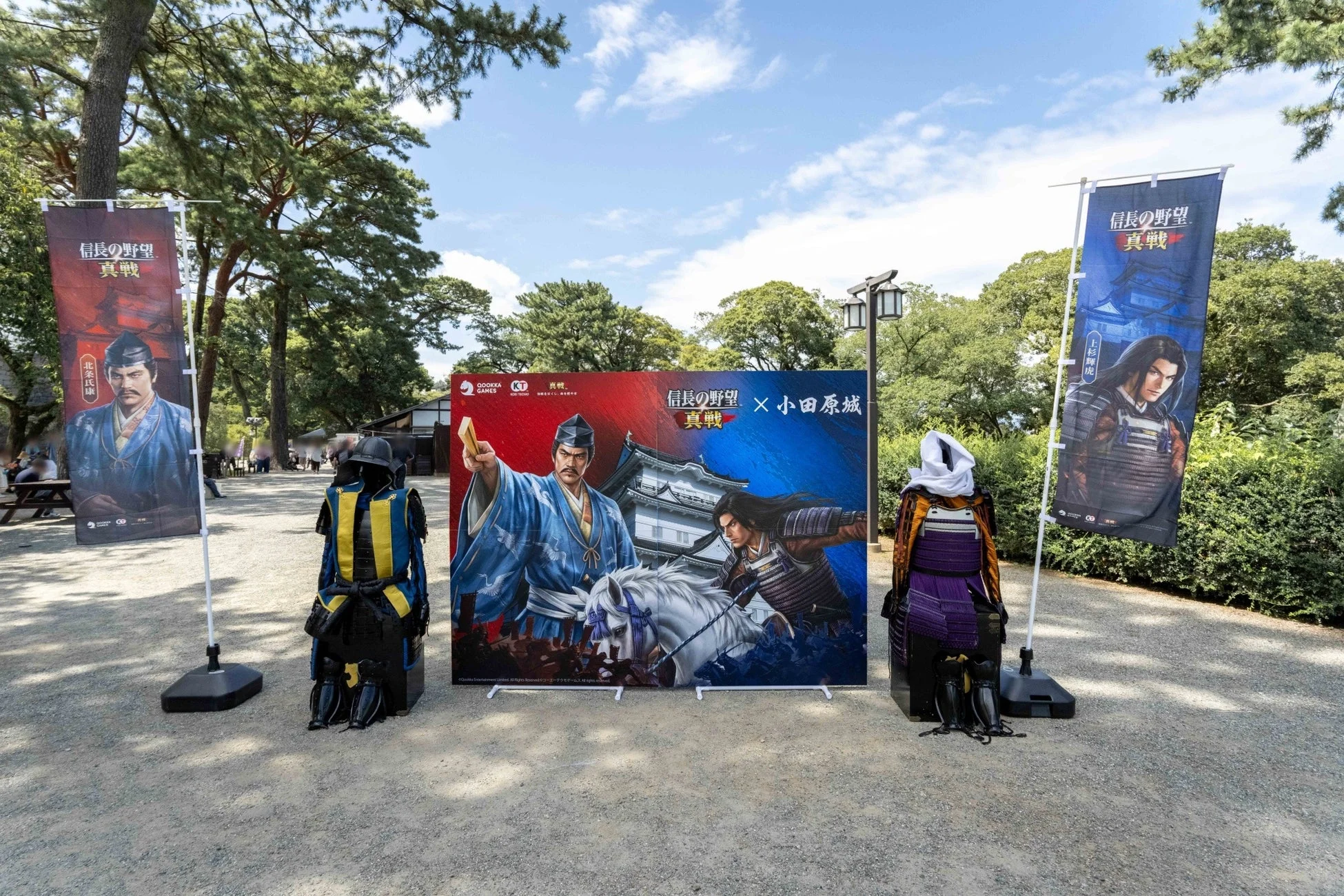 小田原城で開催された「信長の野望 真戦」のコラボイベントの様子。戦国武将のイラストが描かれた大型パネルや旗、そして甲冑が展示されており、歴史とゲームの世界が融合した屋外空間が広がっている。