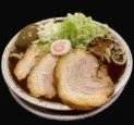 豚骨醤油のような濃い色のスープに浸かったラーメンのクローズアップ画像です。大きなチャーシューが3枚、煮卵、刻みネギ、なるとがトッピングされており、非常に食欲をそそる一品です。
