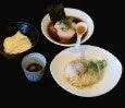 黒い背景に、ラーメンとつけ麺のような2種類の麺料理が並べられています。トッピングにはチャーシューや煮卵、海苔が確認でき、ご飯のようなサイドメニューと小皿のソースも添えられています。