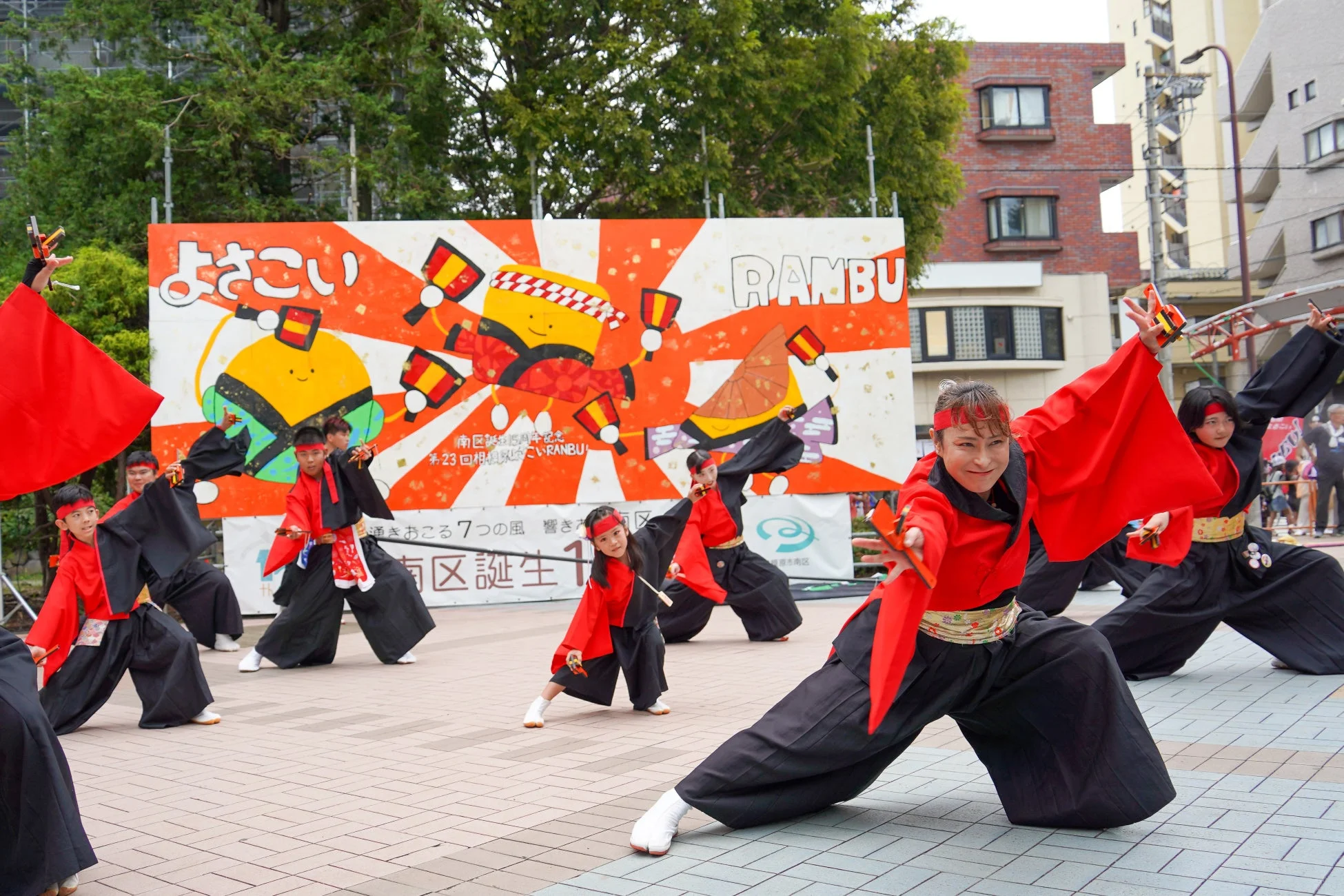 屋外で、赤と黒の衣装を着た人々がよさこい祭りのダンスを披露