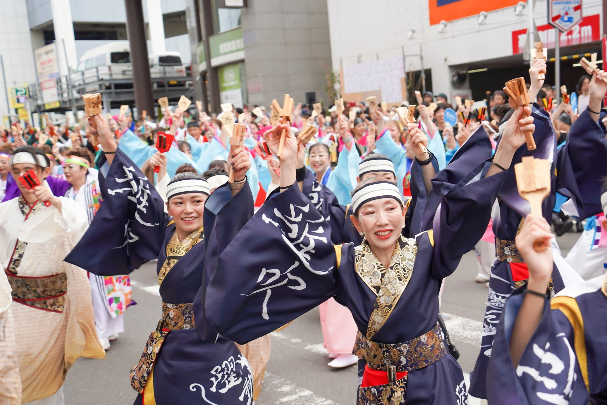 伝統的な衣装を身につけた人々が、木の鳴り物を手に笑顔で踊る日本の祭りの様子
