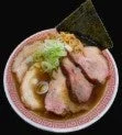 美味しそうなラーメンのクローズアップ画像です。豚肉のチャーシューがたっぷりと盛り付けられ、ネギと海苔が添えられています。