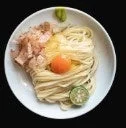 白い器に入った麺料理が上から捉えられています。麺の上には鮮やかな卵黄、削り節、そしてライムがトッピングされており、食欲をそそる一品です。