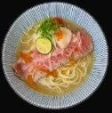 美しい盛り付けのローストビーフラーメンのクローズアップ画像です。透き通ったスープに細麺、薄切りのローストビーフが数枚乗せられ、ライム、ネギ、そしてオレンジ色のイクラのようなものが添えられています。
