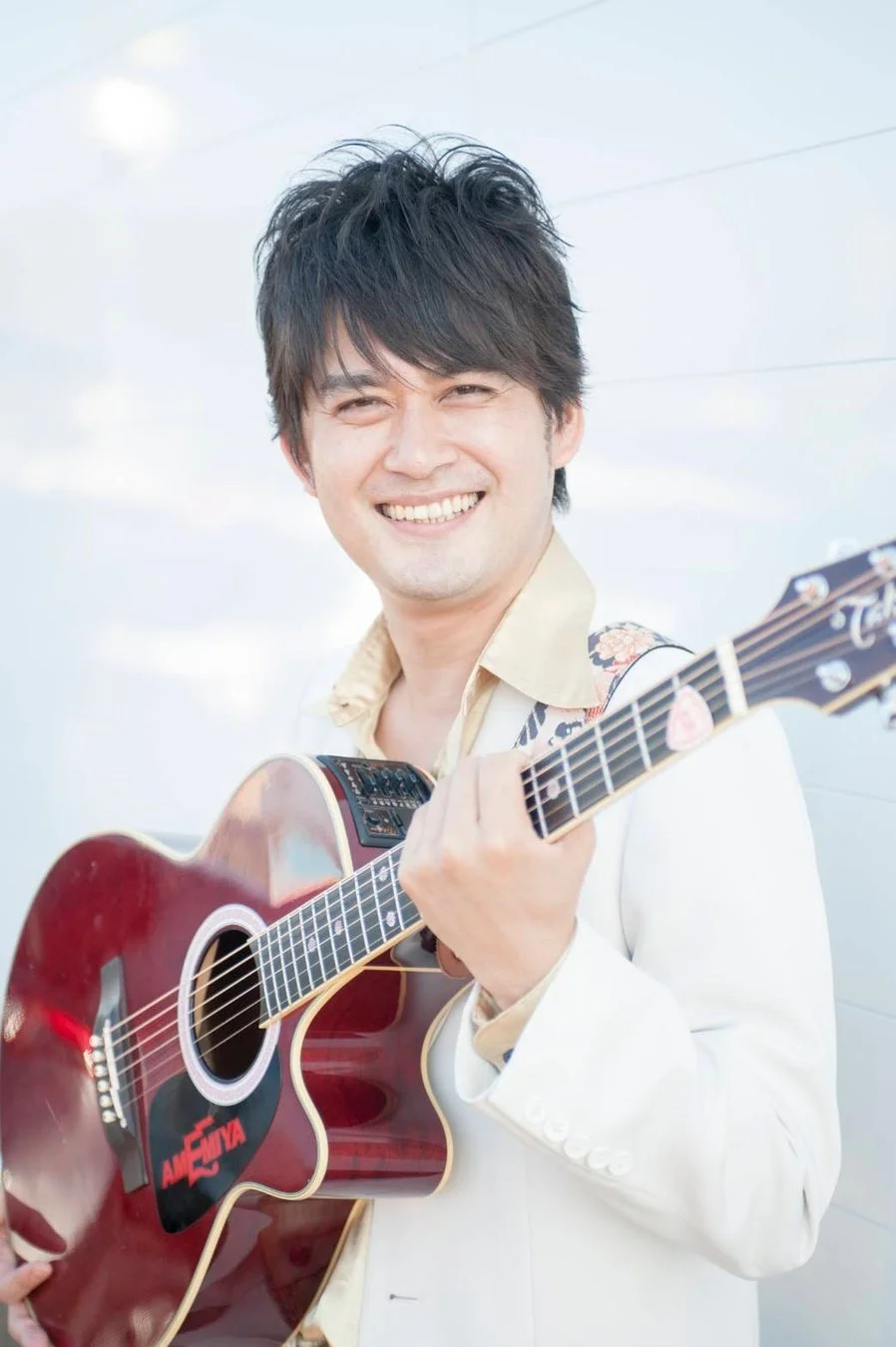 ギターを抱えて笑顔を見せるAMEMIYA