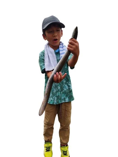 大きなウナギを両手で持ち、驚きと喜びの表情を浮かべる少年。